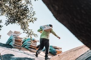 Roofer carrying a bundle of shingles across a roof