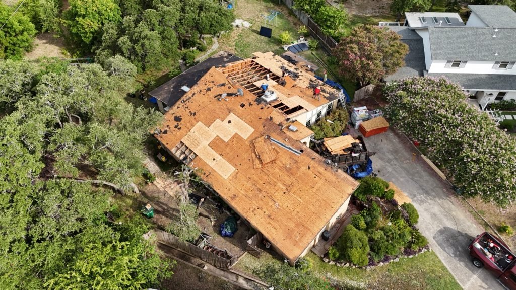 Full roof tear-off with decking exposed and crew working, aerial view